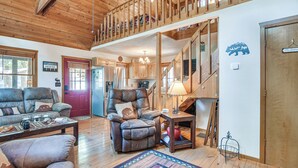 Un salon chaleureux avec une cheminée, un plafond en bois et un escalier menant à l’étage supérieur.