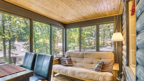 L’intérieur chaleureux d’un chalet, avec un canapé, des fauteuils et de grandes fenêtres donnant sur la forêt environnante.