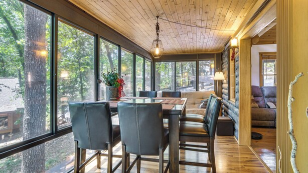 Un espace repas doté d’un plafond en bois, de grandes fenêtres et d’une vue sur les arbres.