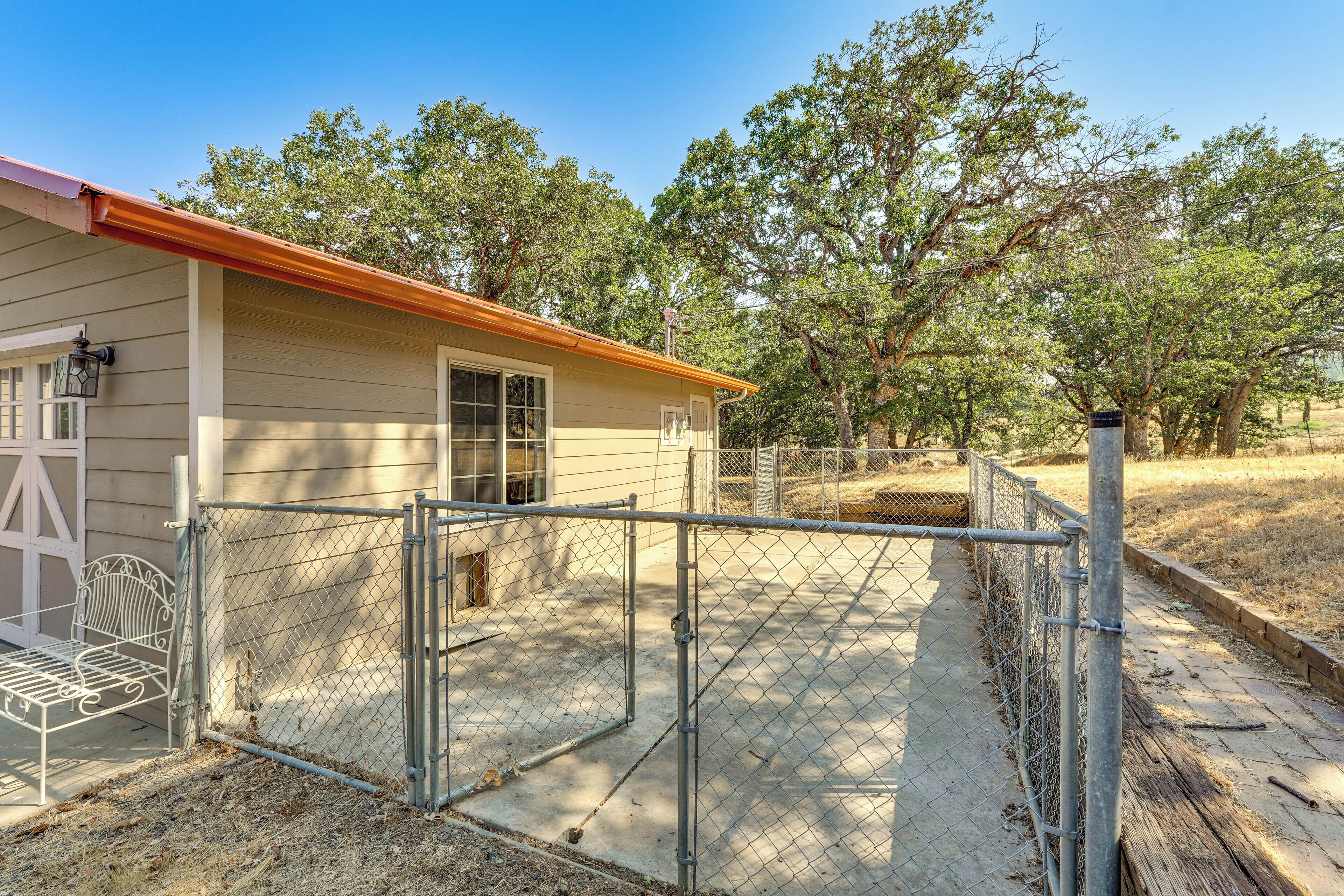 A fenced outdoor area with a metal gate, a bench, and a building with a beige exterior and a red roof.