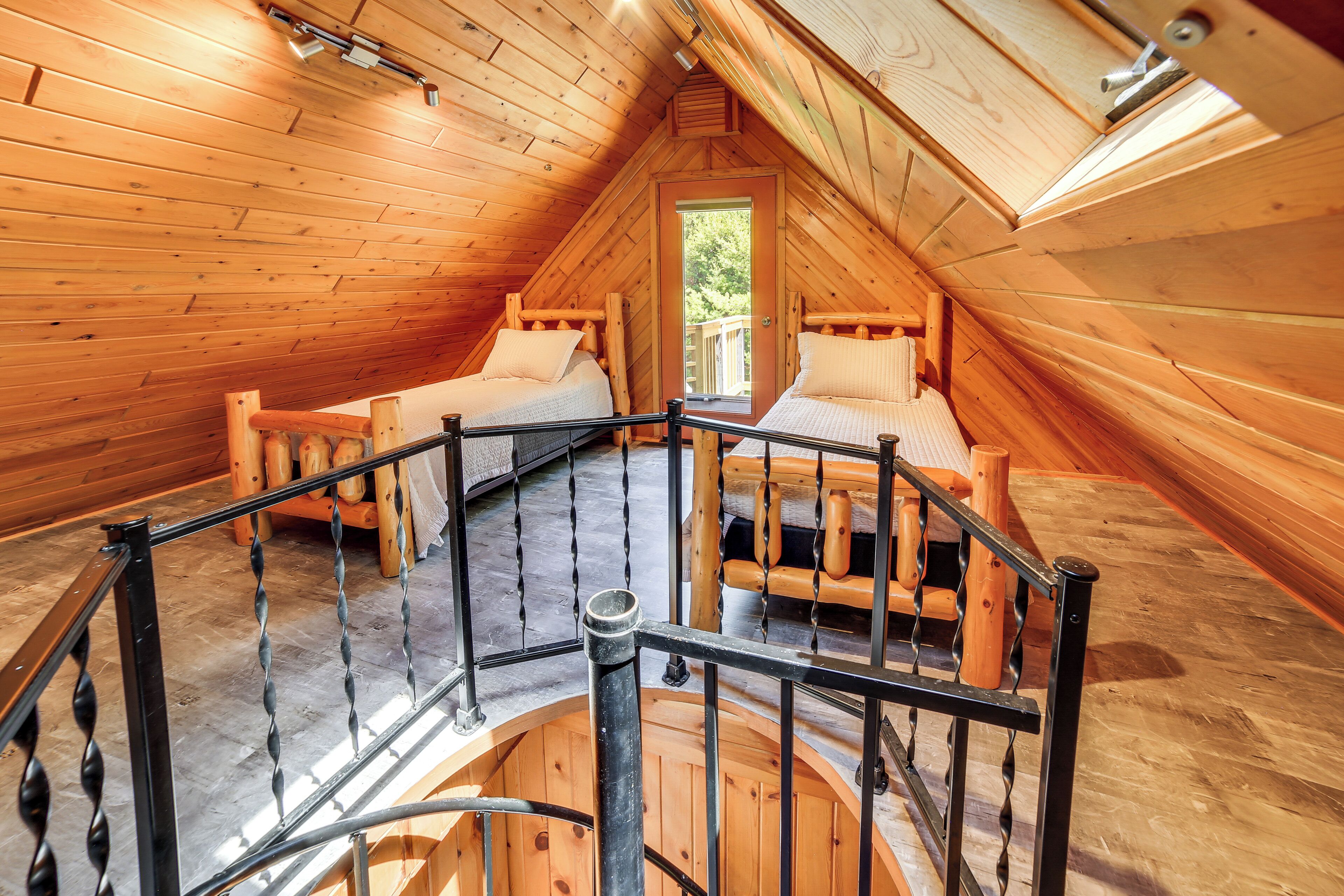 Een houten interieur met een slaapkamer op een entresol, een wenteltrap en een houten terras buiten.