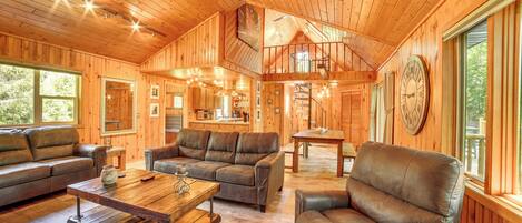 Een ruime houten chalet met slaapkamer op een entresol, een eethoek en een woonkamer met leren banken en een salontafel.