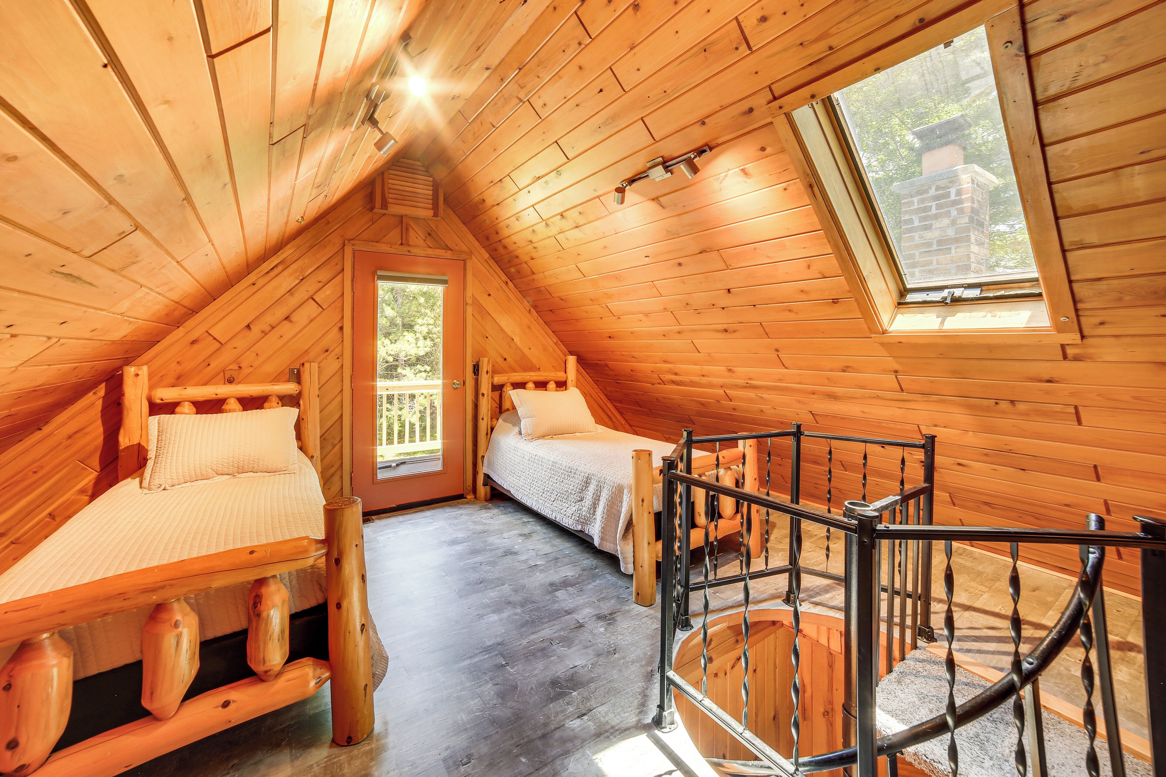 A cozy attic bedroom with two wooden beds, a small window, and a spiral staircase.