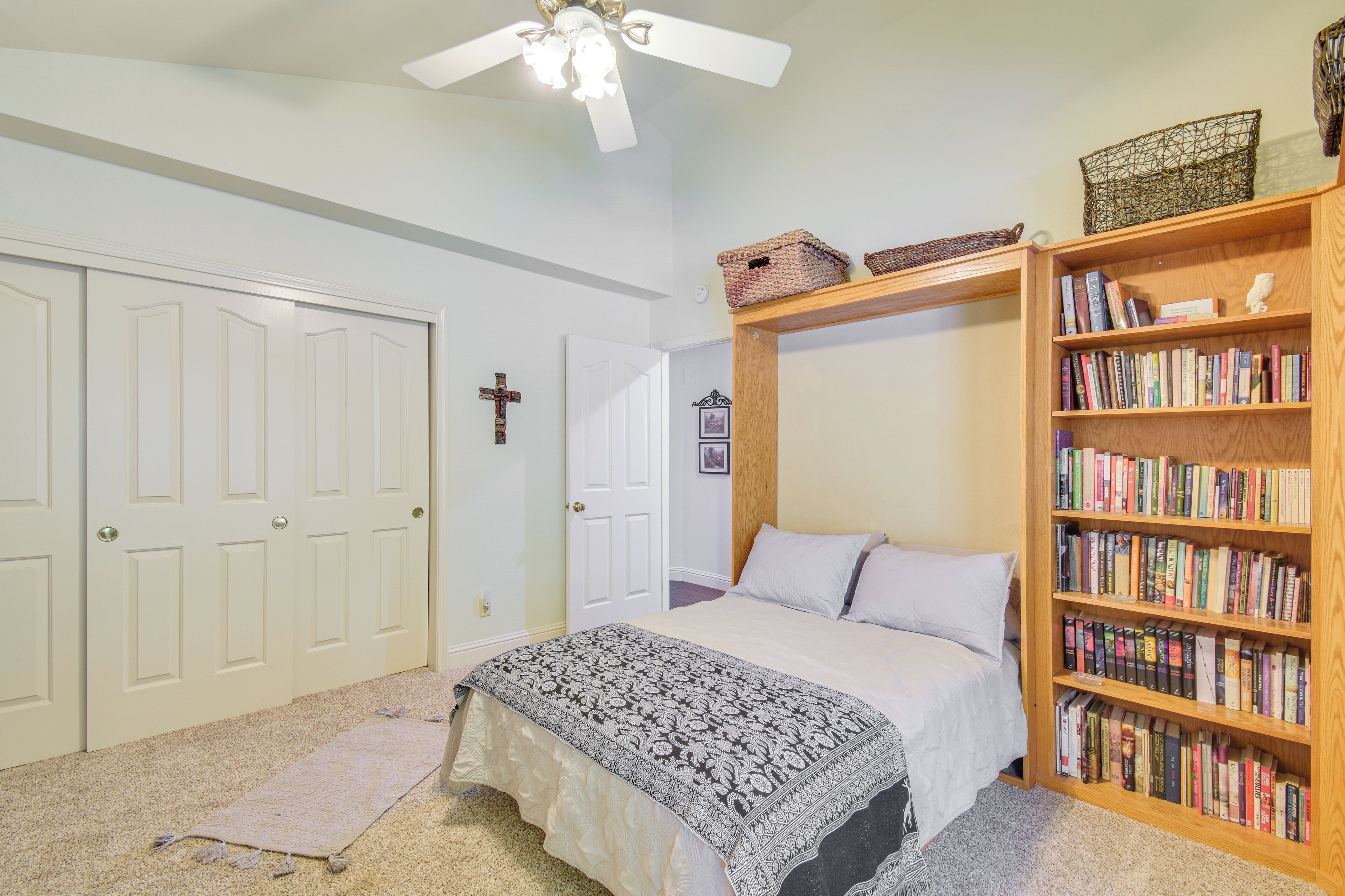 A bedroom with a bed, a bookshelf, a ceiling fan, and a door with a cross on it.