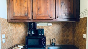 Une cuisine équipée d’un four à micro-ondes, d’une machine à café et d’un grille-pain sur le plan de travail, d’un évier et de placards en bois au-dessus.