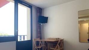 Une pièce avec une table et des chaises en bois, un téléviseur fixé au mur et une porte donnant sur un espace extérieur.