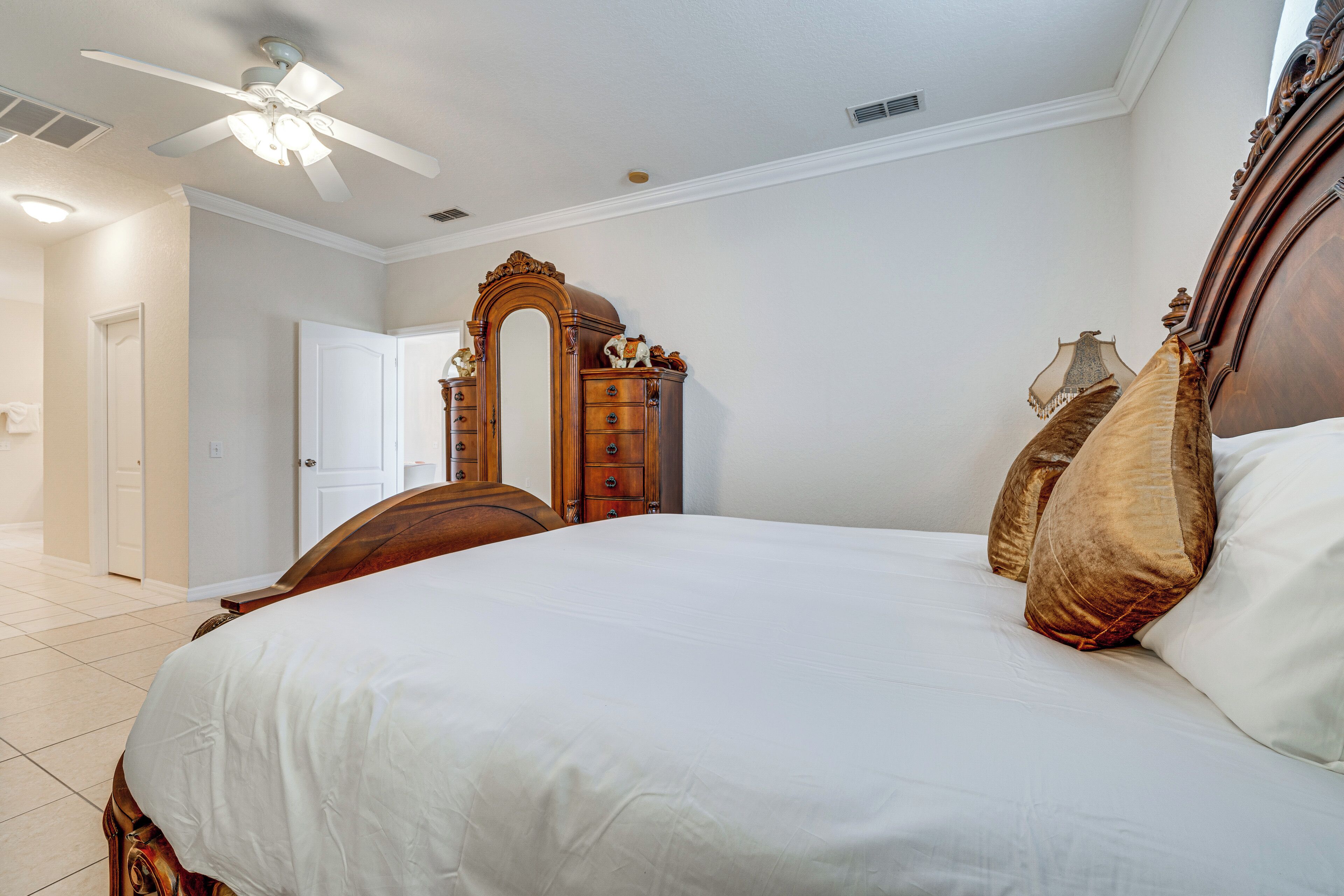 A bedroom with a large bed, a wooden dresser, a mirror, and a ceiling fan.