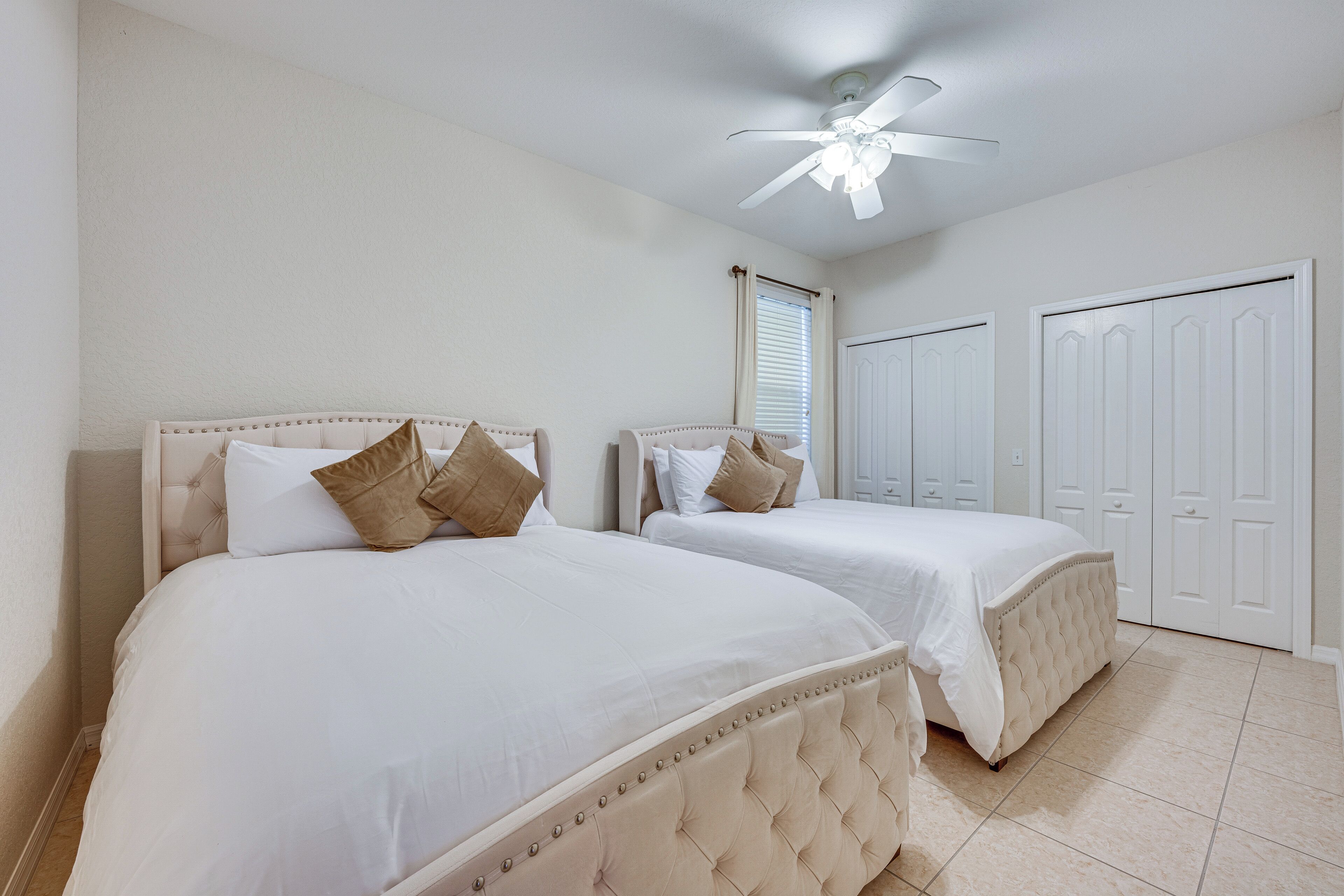 A bedroom with two beds, a ceiling fan, and a window with blinds.