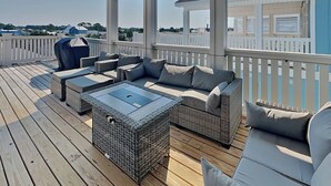Eine überdachte Terrasse im Freien mit Korbmöbeln, einem Tisch mit Glasplatte und Blick auf die Umgebung.