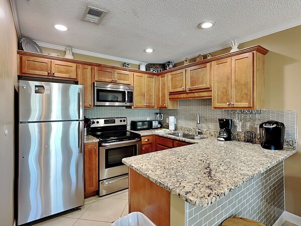 A modern kitchen with stainless steel appliances, wooden cabinets, and a granite countertop. - Crystal Beach Condo, Community Pool, Across from the Beach! (Destin)