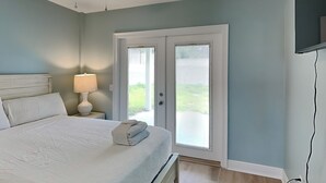 A bedroom with a bed, nightstand, lamp, ceiling fan, and a door leading outside. - PC Beach Retreat A | 0.5mi to Beach, Outdoor Showers, Shard Yard (Panama City Beach)