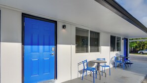 A building with a blue door, white exterior walls, and a covered outdoor seating area with blue chairs and tables. - Pet-friendly Hallandale Beach Condo Near Boardwalk (Hallandale Beach)