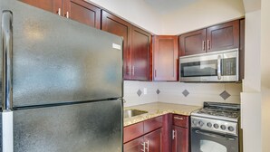 A kitchen with a stainless steel refrigerator, a microwave, a stove, and wooden cabinets. - Pet-friendly Hallandale Beach Condo Near Boardwalk (Hallandale Beach)