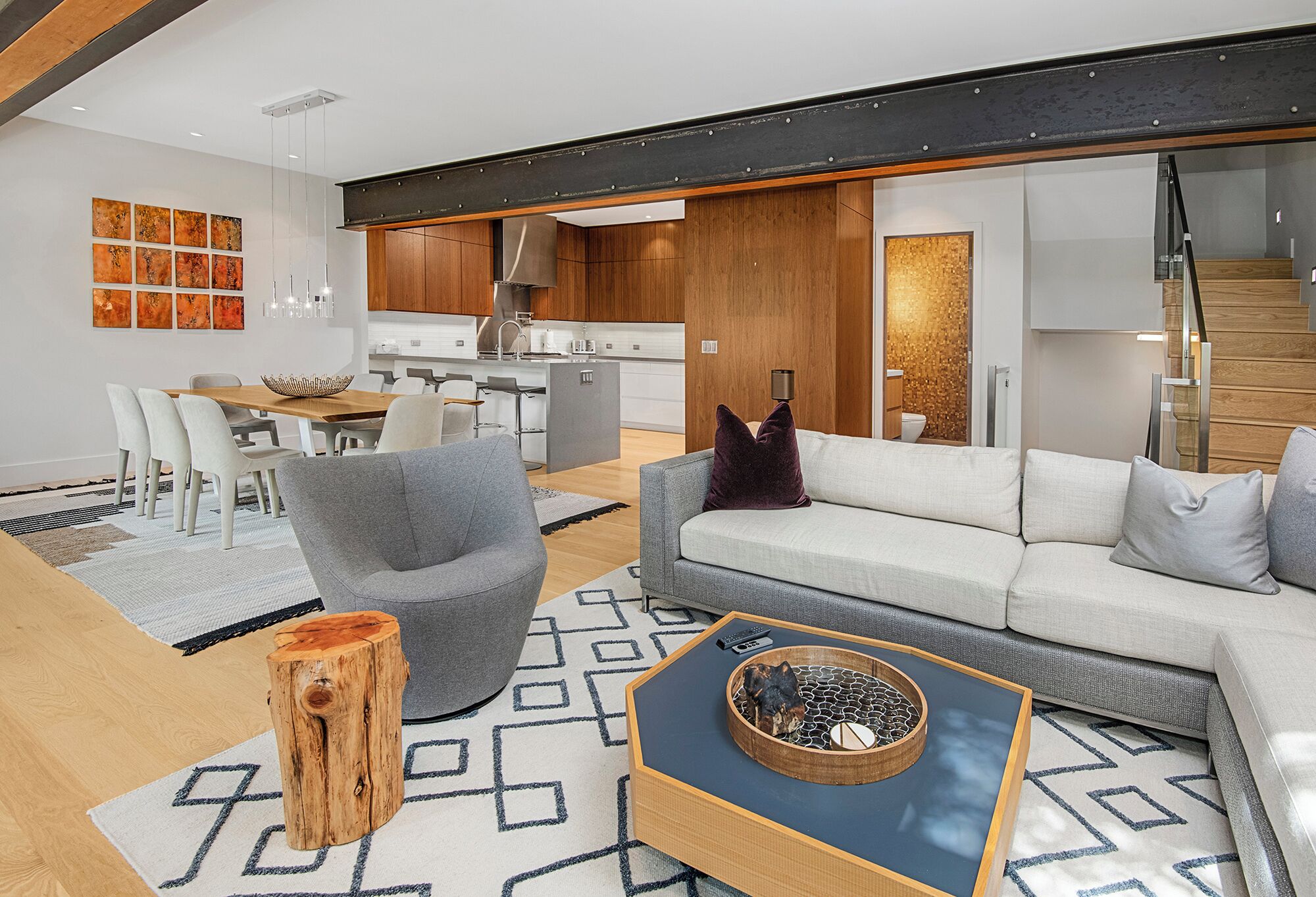 A modern living room with a grey sofa, a wooden coffee table, and a dining area with a white table and chairs.