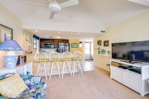 A living room with a sofa, a TV, a ceiling fan, and a kitchen in the background. - Pool Access & Close to Beach: Myrtle Beach Condo (Myrtle Beach)