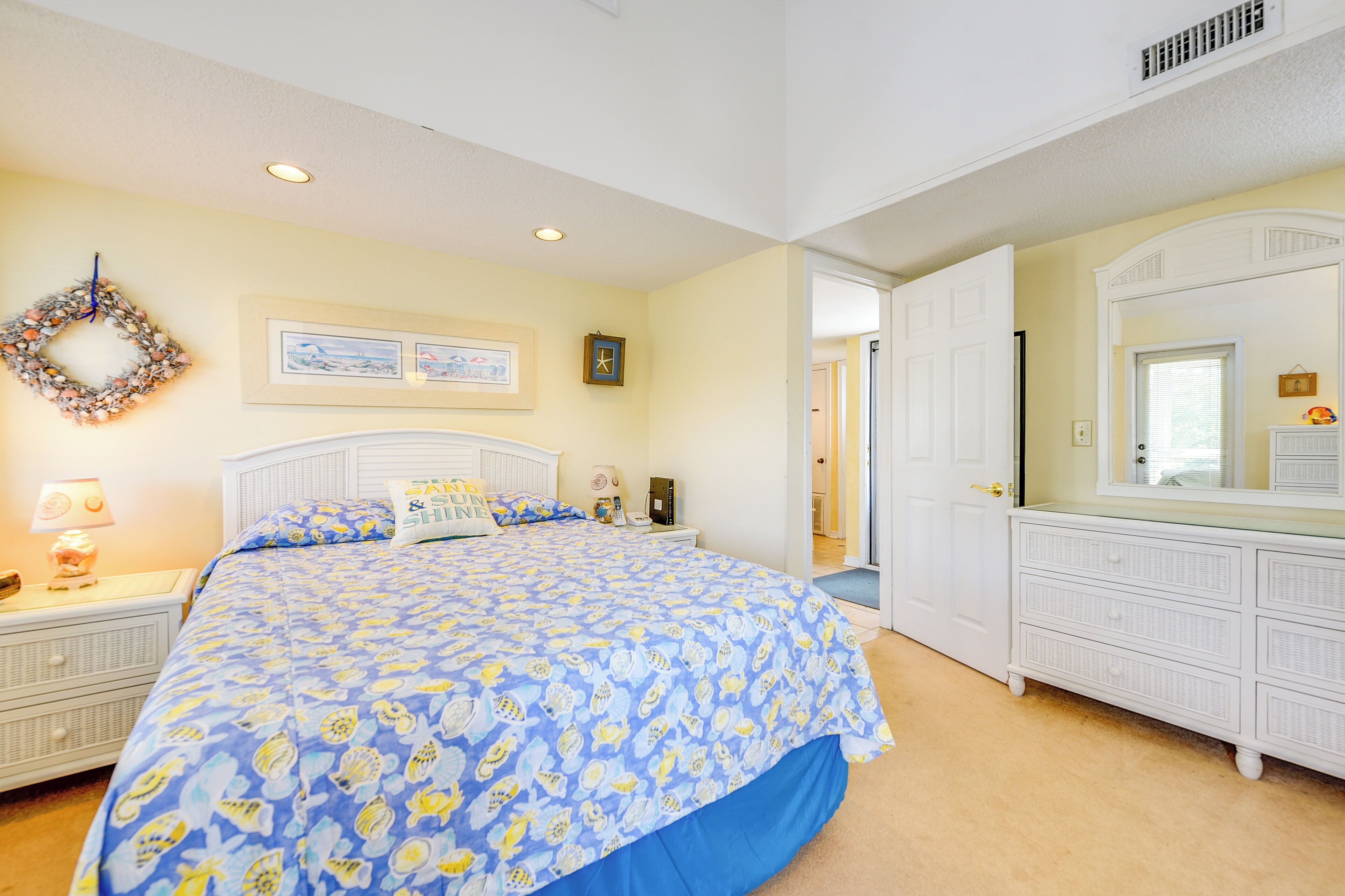 A bedroom with a large bed, a dresser, a nightstand, a wall clock, and a framed picture.