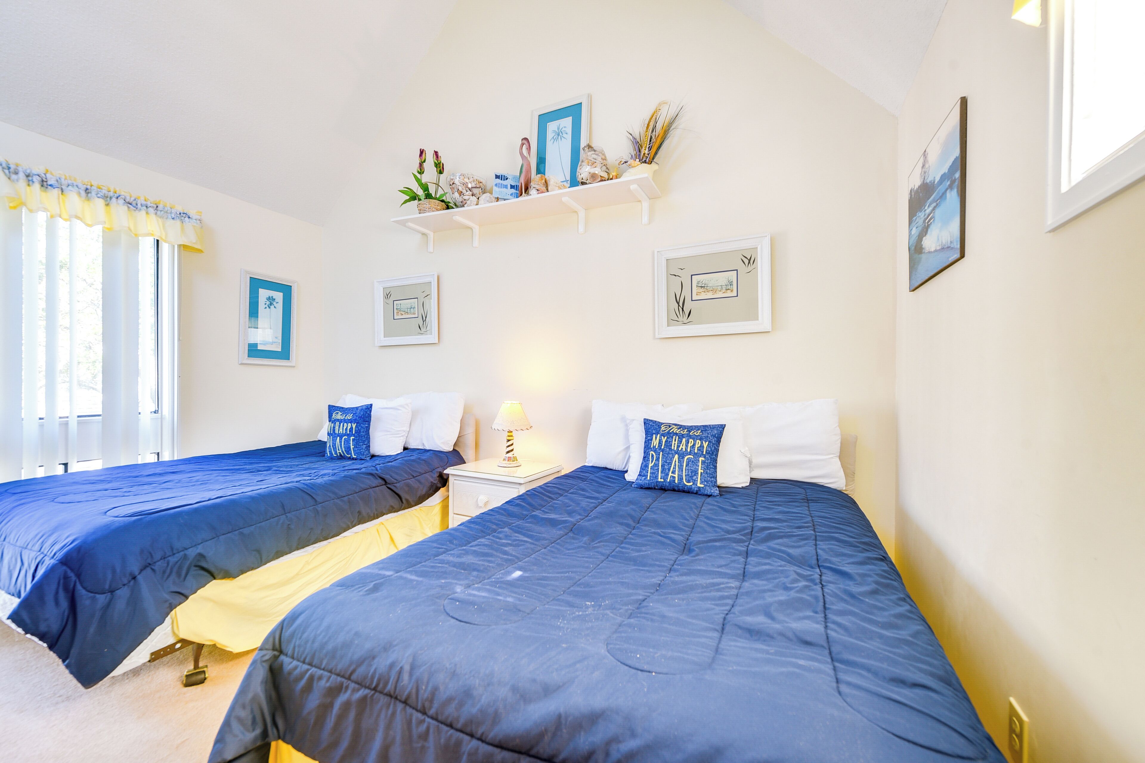 Une chambre avec deux lits, une étagère ornée d’objets décoratifs et des tableaux encadrés accrochés au mur.