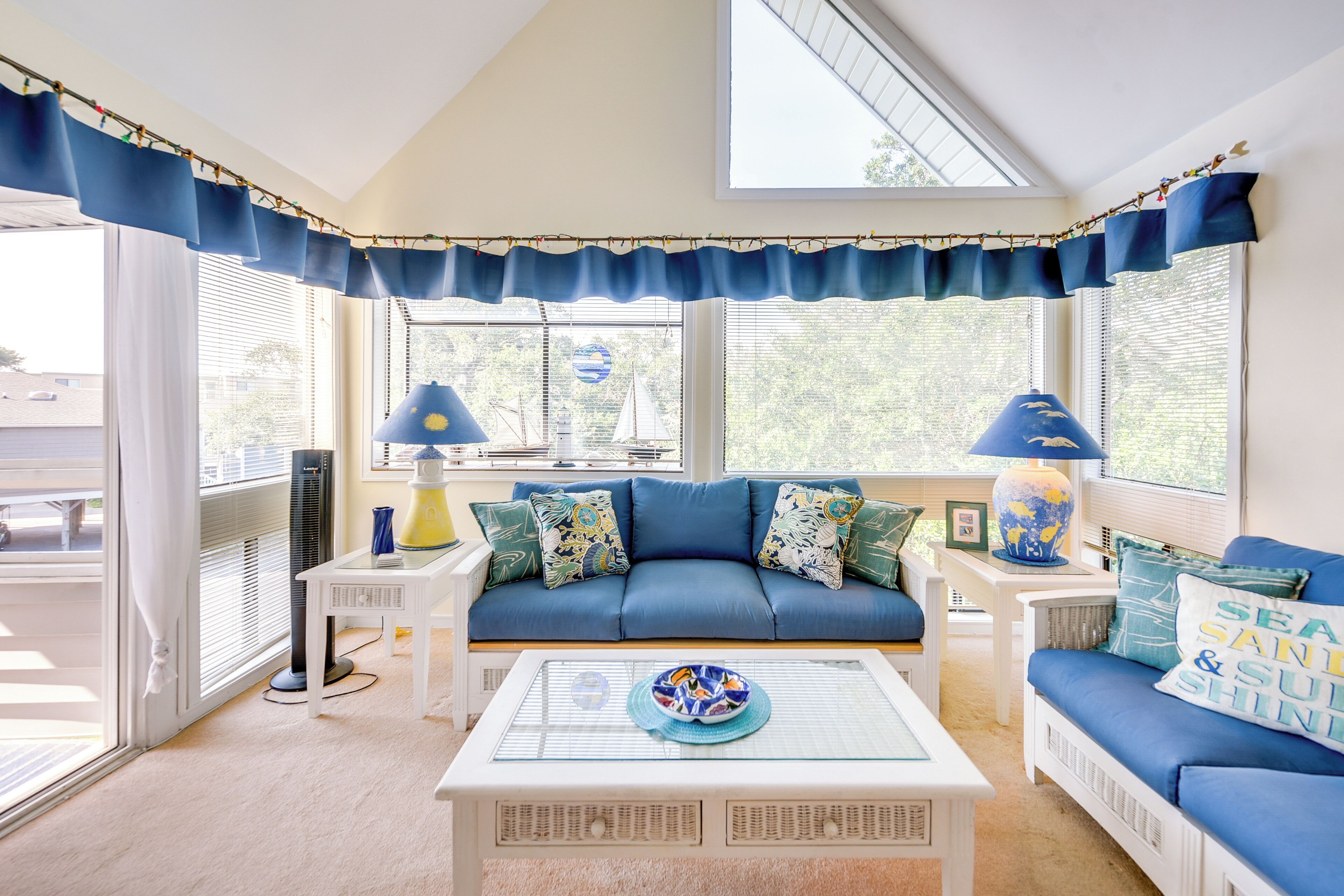 A room with a blue sofa, white coffee table, and a view of the outdoors.