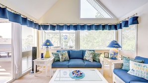 A room with a blue sofa, white coffee table, and a view of the outdoors.