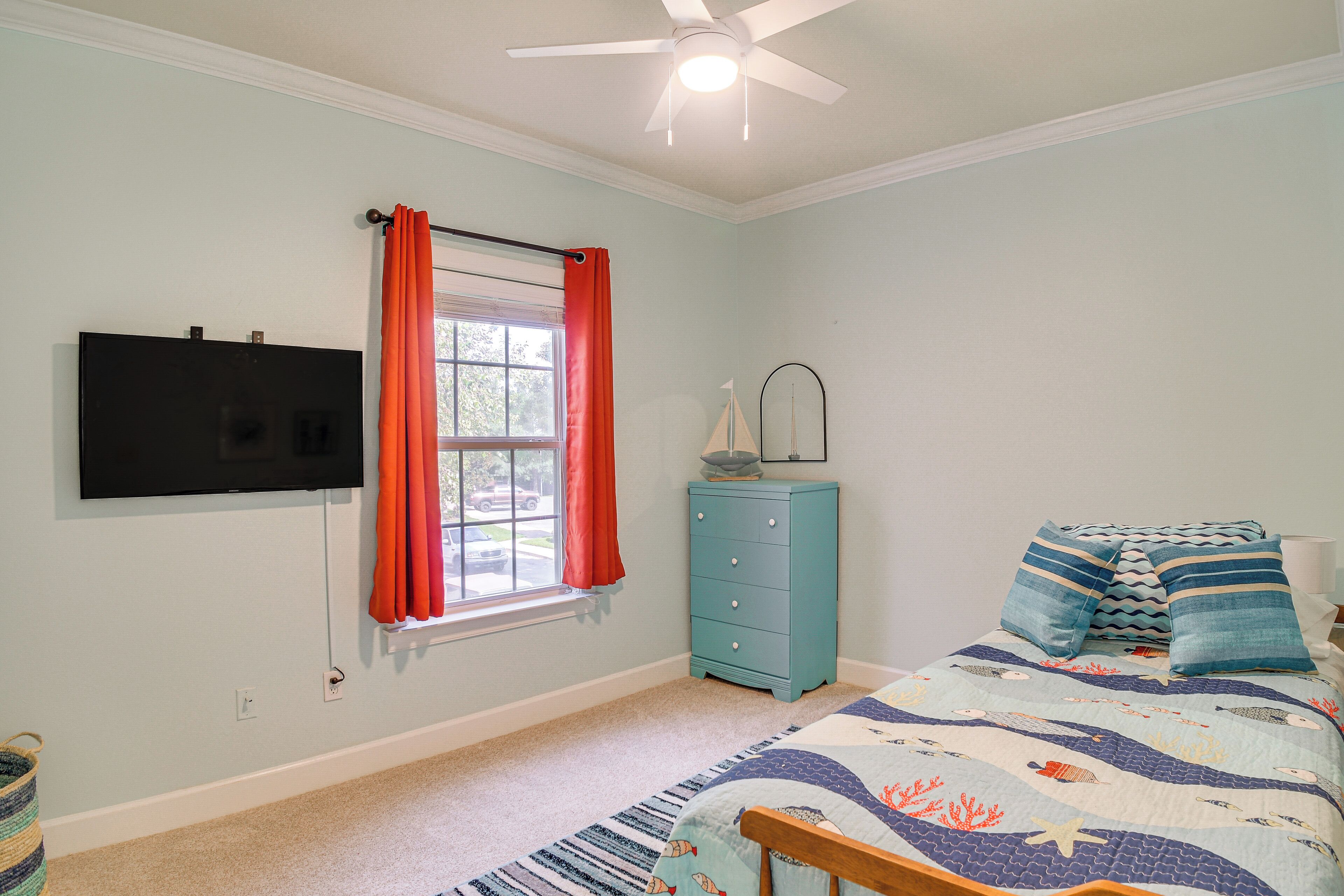 A bedroom with a bed, a dresser, a television, and a window with curtains.