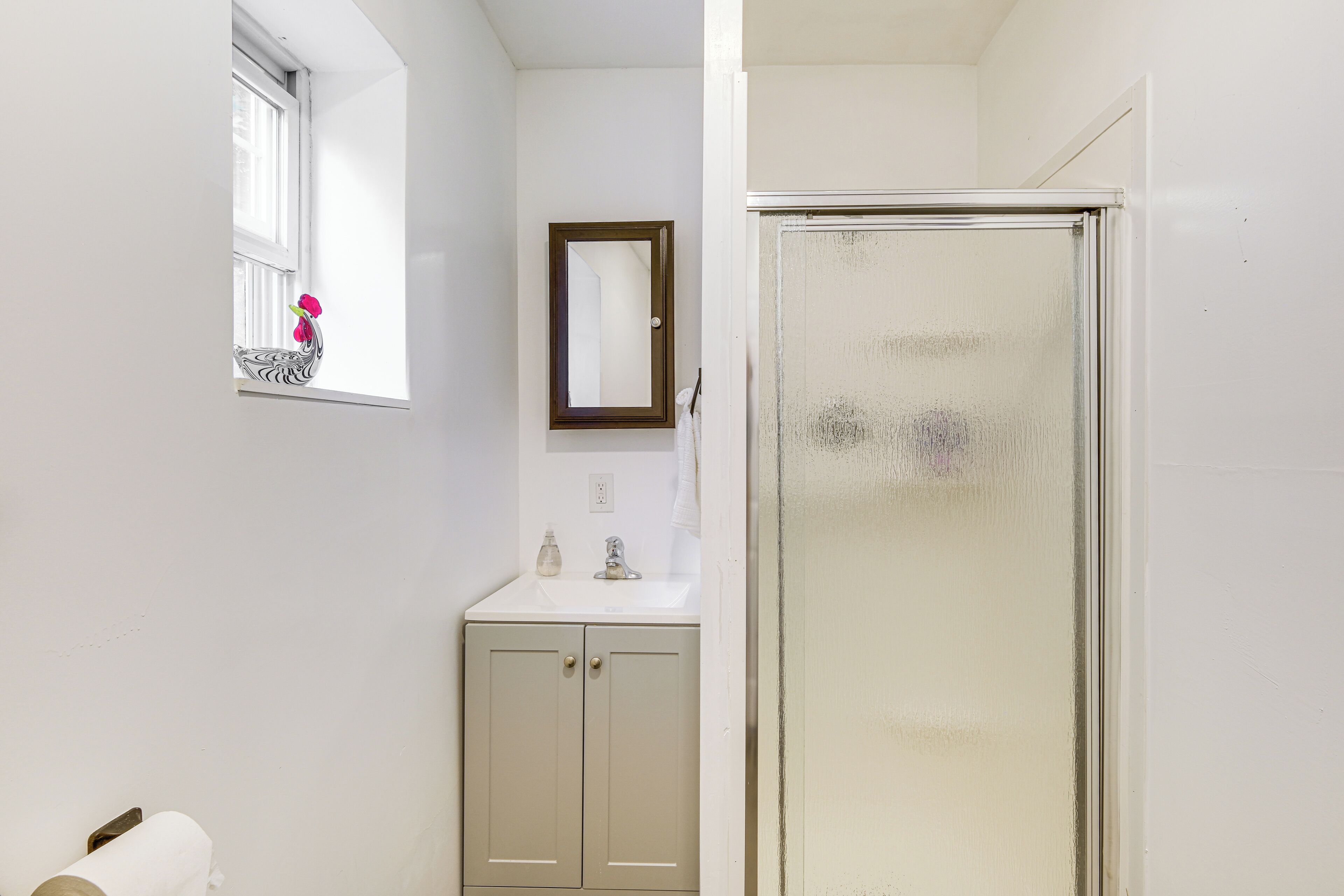 Een badkamer met een raam, een spiegel, een wastafel en een douche.