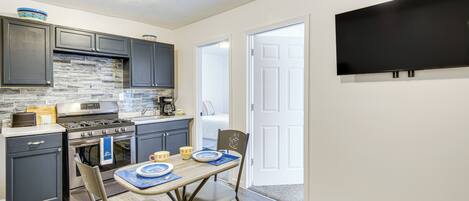 A compact kitchen with dark cabinets, a built-in stove, and a flat-screen TV mounted on the wall.