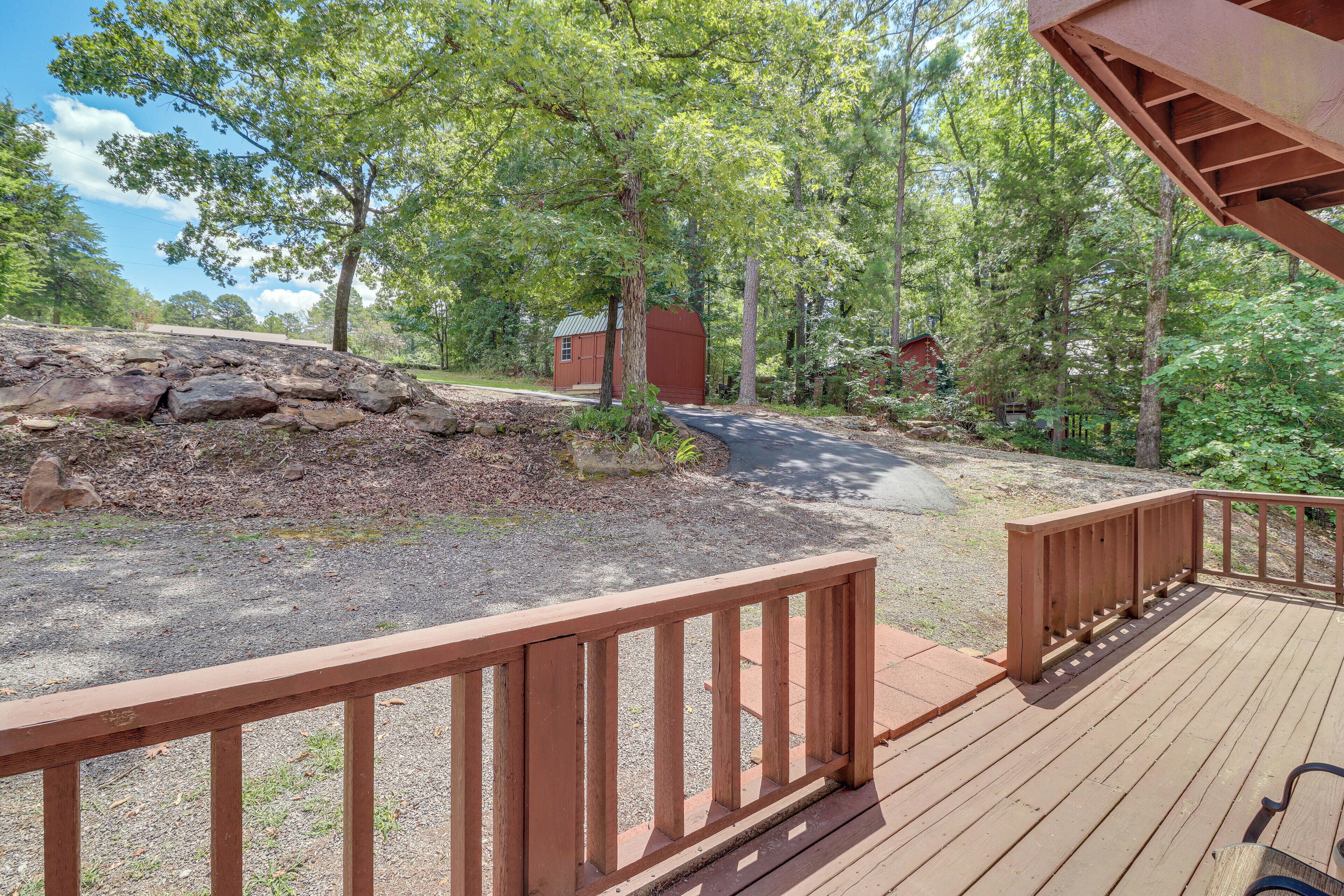 A wooden deck with a stone wall and a small building in a wooded area.