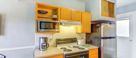 A kitchen with wooden cabinets, a stainless steel refrigerator, a microwave, a stove, and a coffee maker.