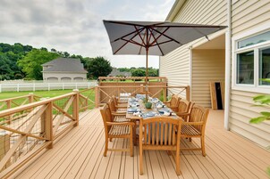 An outdoor wooden deck with a table set for dining, surrounded by chairs, and an umbrella.
