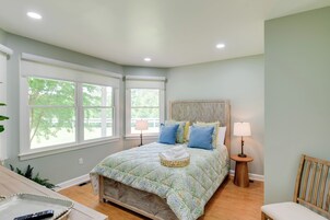 A bedroom with a large bed, two bedside lamps, a wooden headboard, and a window with a view of trees.