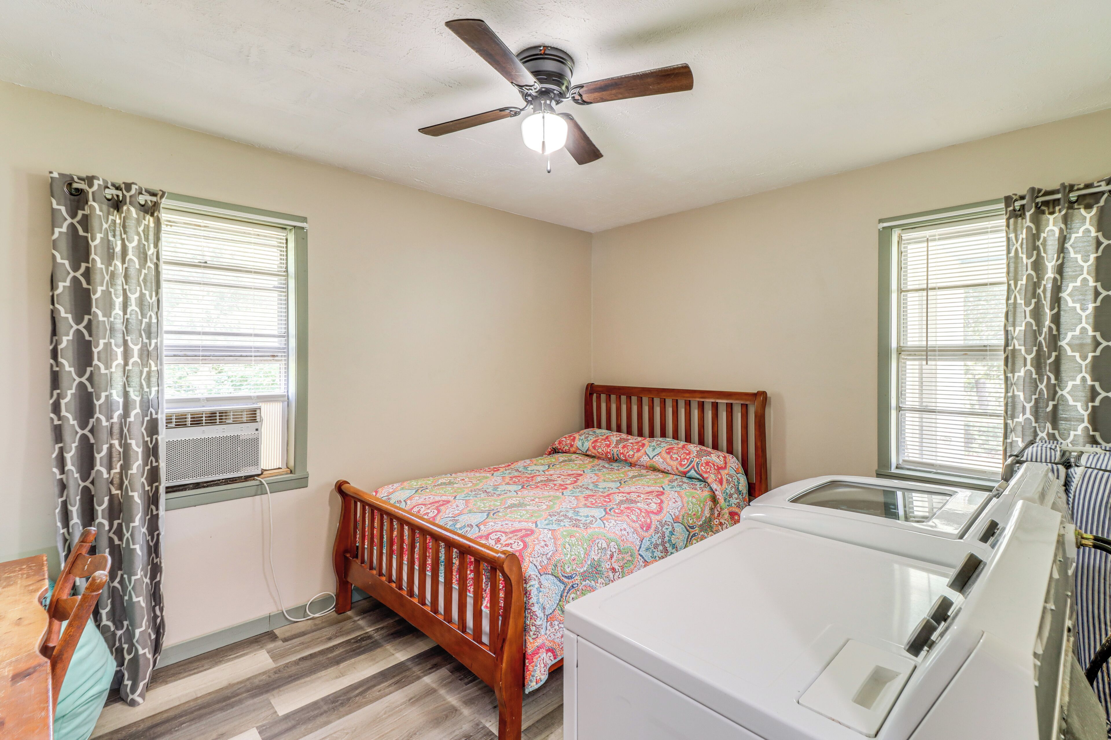 A bedroom with a wooden bed, a ceiling fan, an air conditioning unit, and a washing machine.