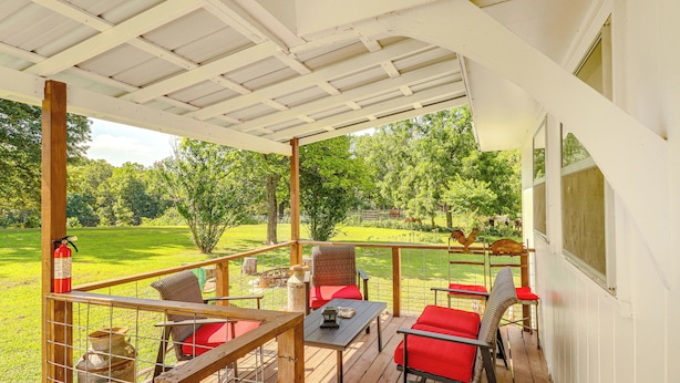A covered outdoor patio with wooden flooring, red and black outdoor furniture, and a view of a green landscape. - Horses Welcome: Marble Falls Home w/ Grill! (Marble Falls)