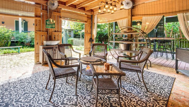 Une terrasse couverte, aménagée avec des meubles en osier, un ventilateur et offrant une vue sur le jardin.
