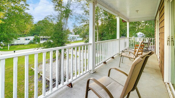 A covered porch with white railings, two wicker chairs, and a view of a green lawn and a trailer in the background. - Half Mile to Beach: Murrells Inlet Home w/ Deck! (Murrells Inlet)