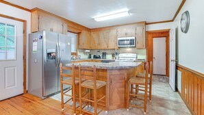 A kitchen with wooden cabinets, a stainless steel refrigerator, a microwave, and a bar area with stools. - Half Mile to Beach: Murrells Inlet Home w/ Deck! (Murrells Inlet)