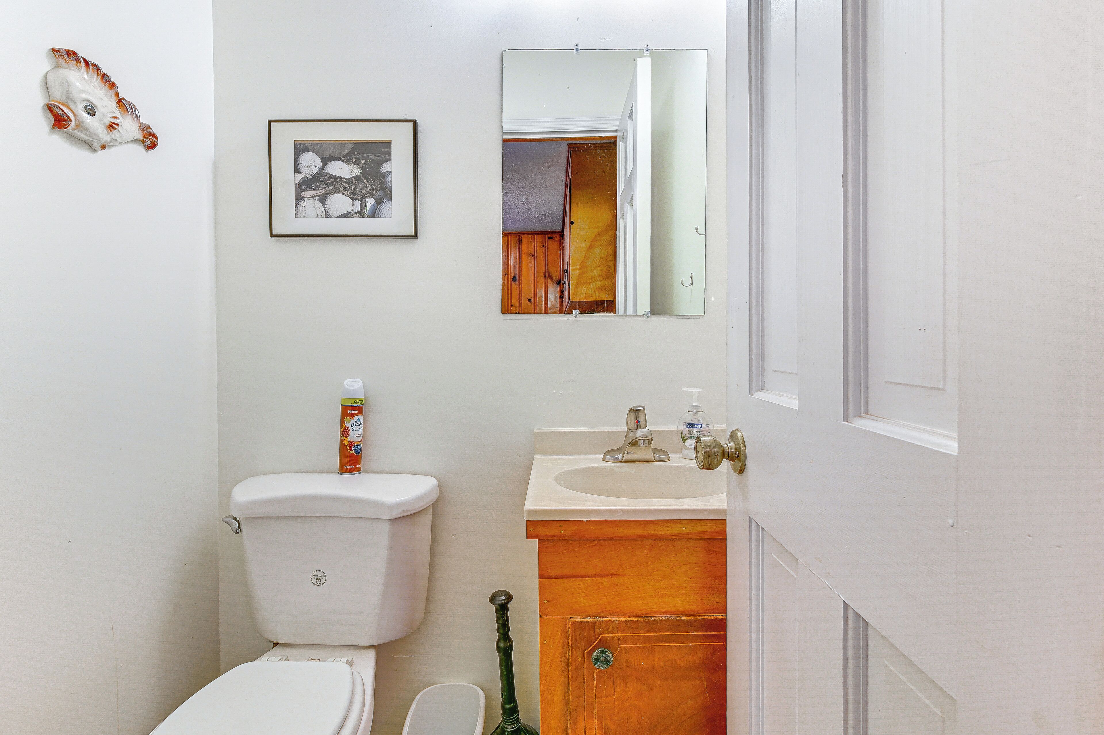A bathroom with a toilet, sink, mirror, and a framed picture on the wall.