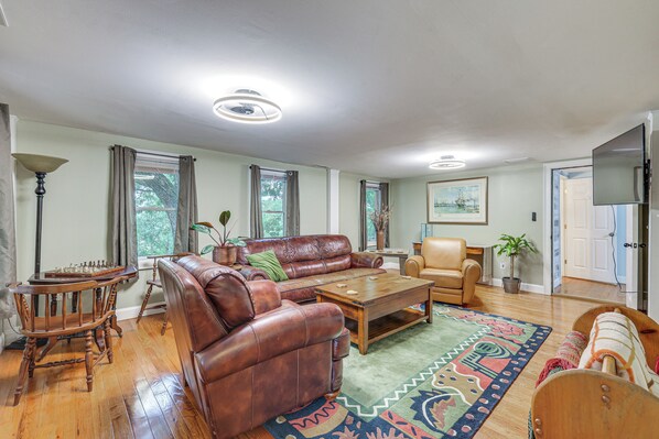 A spacious living room with a leather sofa, wooden coffee table, and a patterned rug. - Quintessential New England Home w/ Patio & Grill! (Putnam)