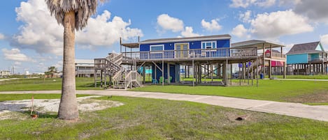 Una casa frente a la playa con una terraza de madera y una escalera que conduce a la entrada principal.