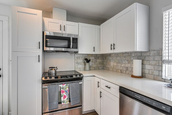 A modern kitchen with white cabinets, a stainless steel stove, a microwave, and a dishwasher. - Walk to Sand: Surfside Beach Getaway w/ Deck (Freeport)