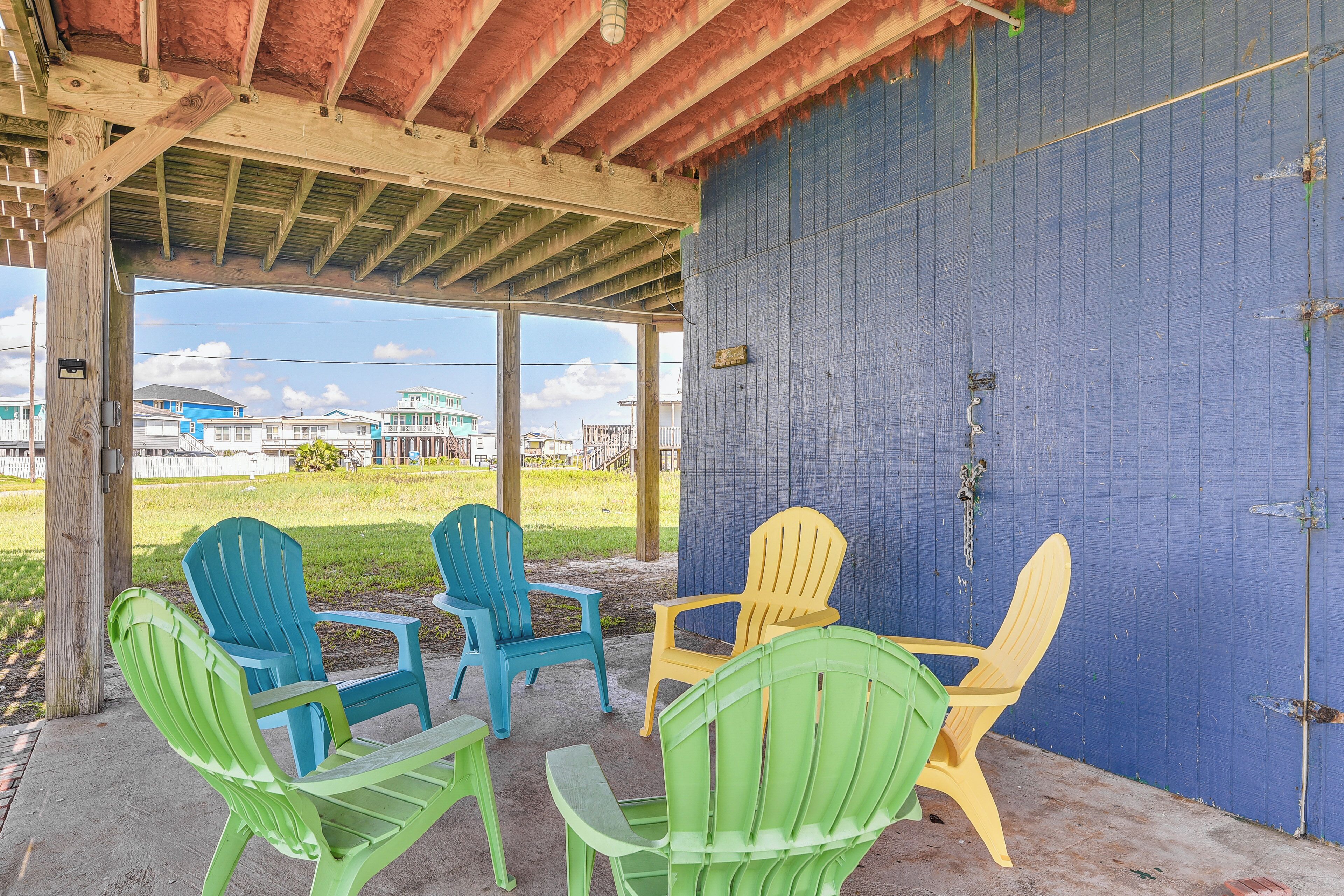 A covered outdoor seating area with four Adirondack chairs in green, blue, and yellow.
