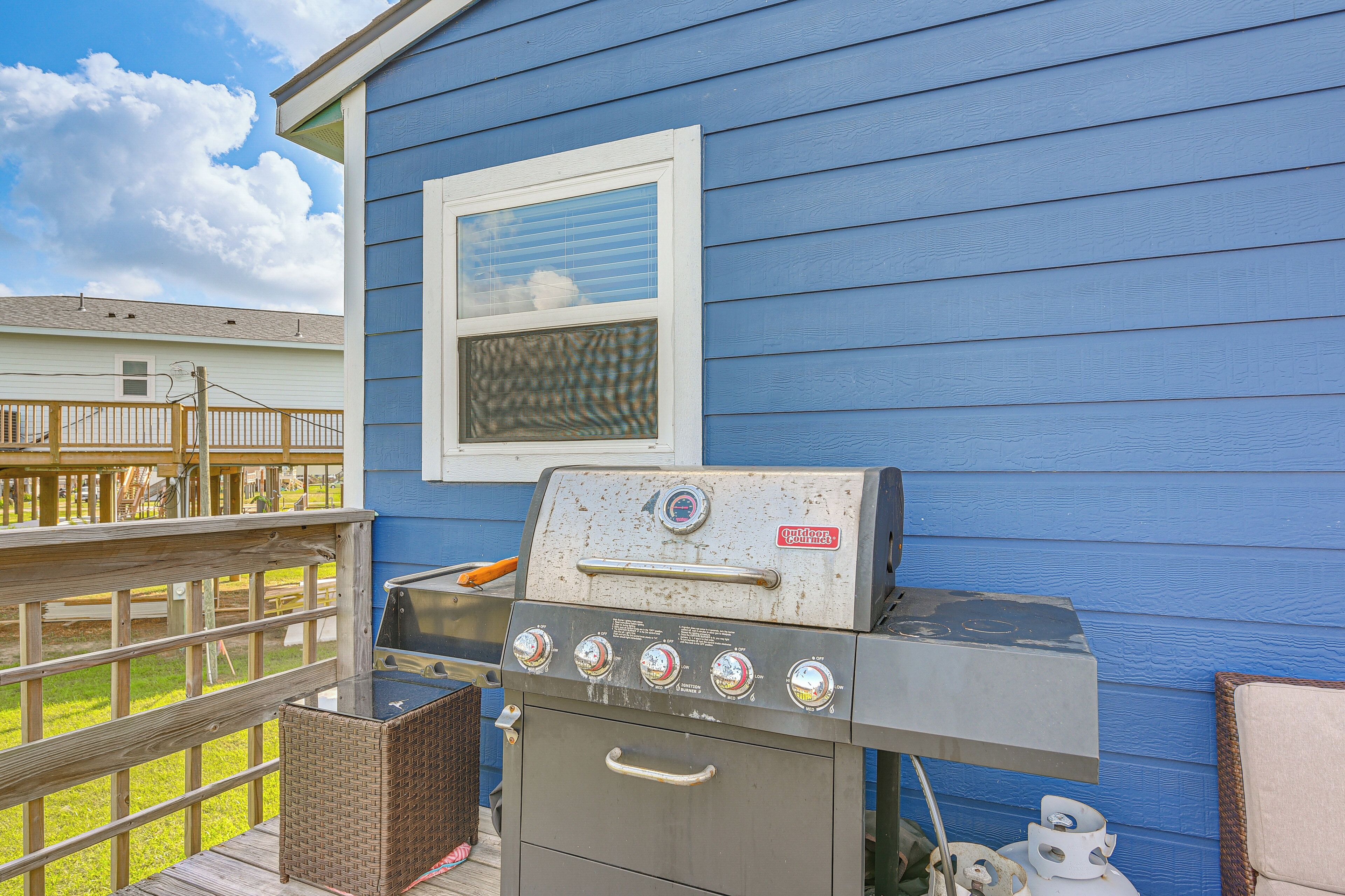 A barbecue grill in front of a blue house with a window.