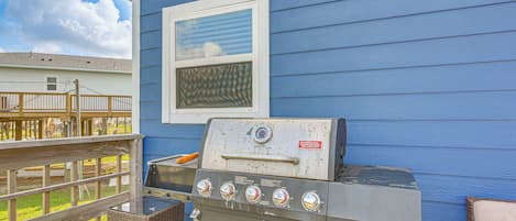 A barbecue grill in front of a blue house with a window.