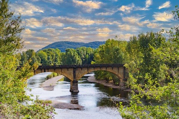 Un pont de pierre enjambe une rivière, bordée d’arbres de chaque côté.