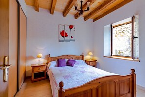 A bedroom with a wooden bed, bedside tables with lamps, a stone wall, and a window.