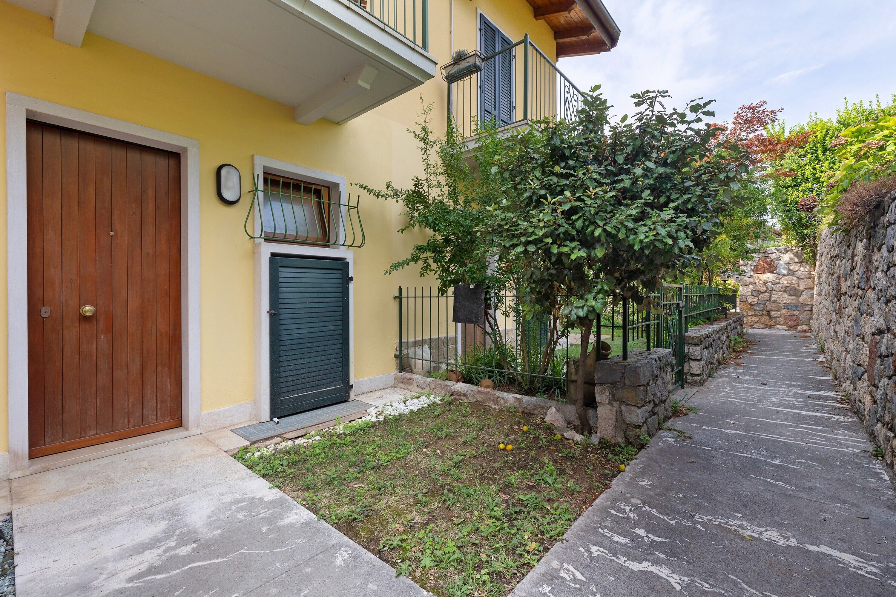 Un edificio giallo con una porta in legno, una finestra con persiane verdi e un muro in pietra.