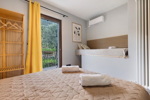 A bedroom with a bed, a wooden wardrobe, a yellow curtain, a framed picture, and a window with a view of greenery.