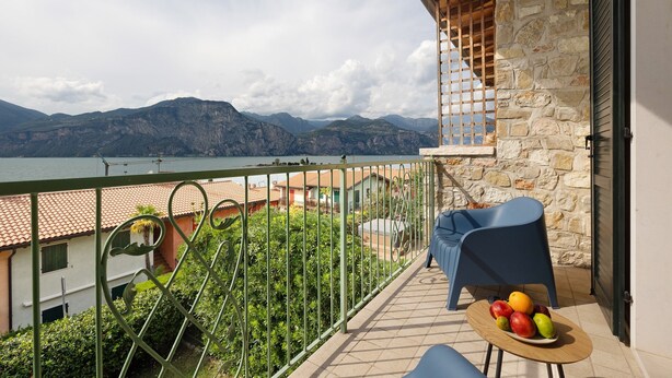 A balcony with a view of mountains, a table with fruit, and a chair. - Holiday Home 'Casa Di Tino' with Lake View, Wi-Fi and Air Conditioning (Brenzone sul Garda)