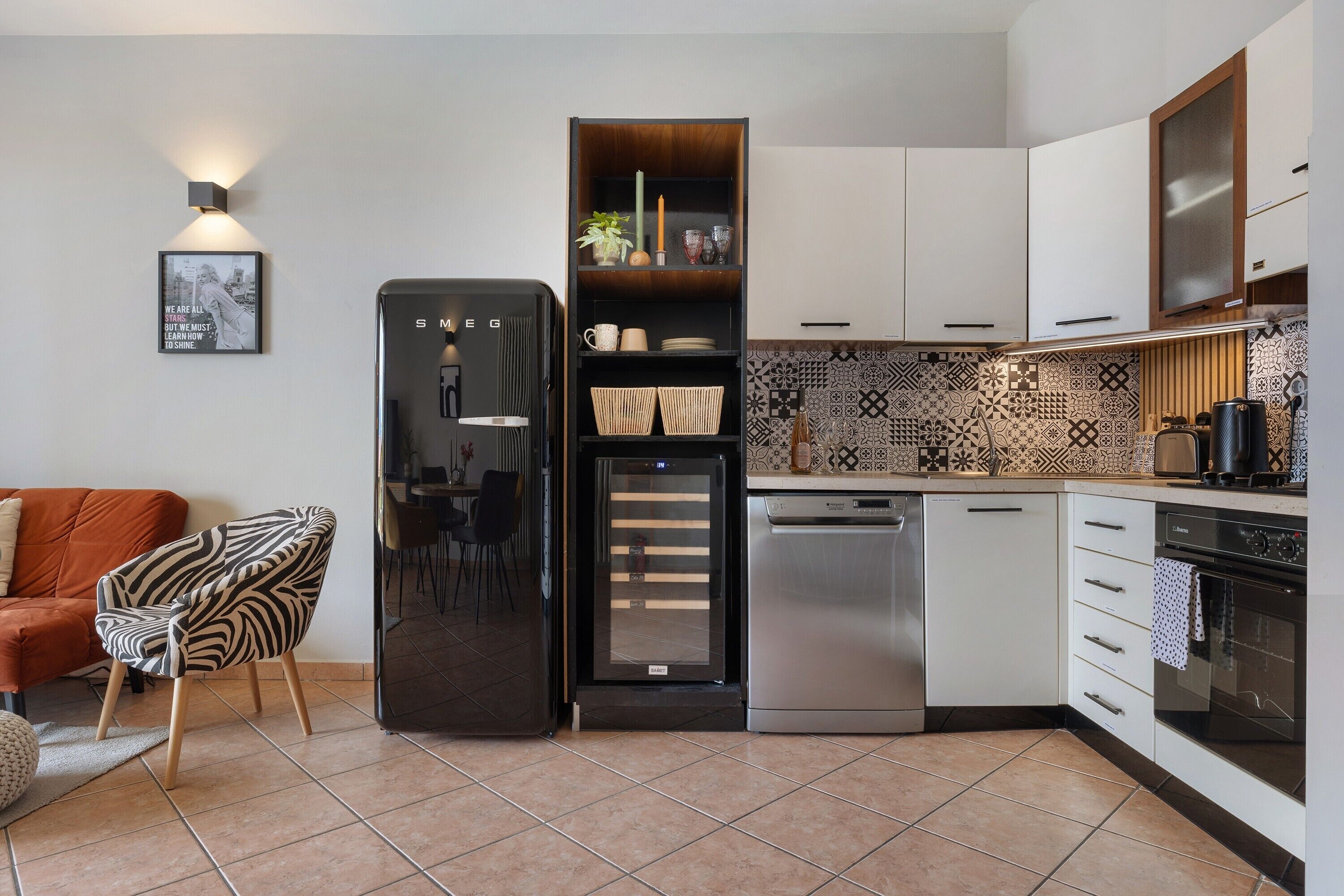 Eine kleine Küche mit Kühlschrank, Geschirrspüler, Backofen und einer Wandfliese mit Muster.