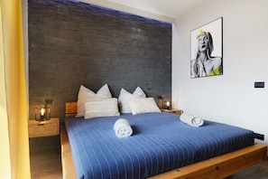 A bedroom with a wooden bed frame, a blue striped bedspread, and a wall-mounted artwork.