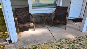 A porch with two wicker chairs and a small round table, a window with blinds, and a door. - 3 blocks to Notre Dame, EV Charger, BBQ & Fire Pit! (1707) (South Bend)